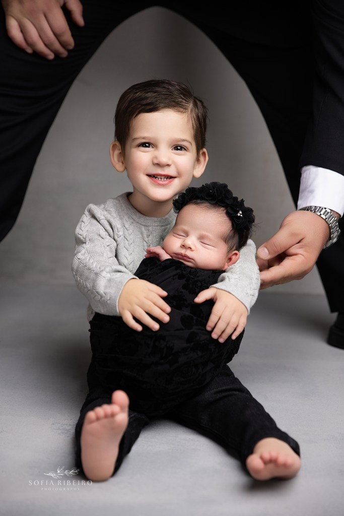 big brother holds onto his baby sister with help from dad during a newborn photo shoot