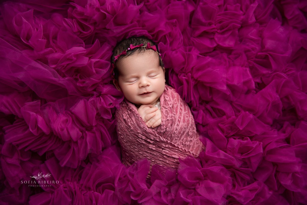 newborn baby girl rests in a bed of pink tulle ruffles