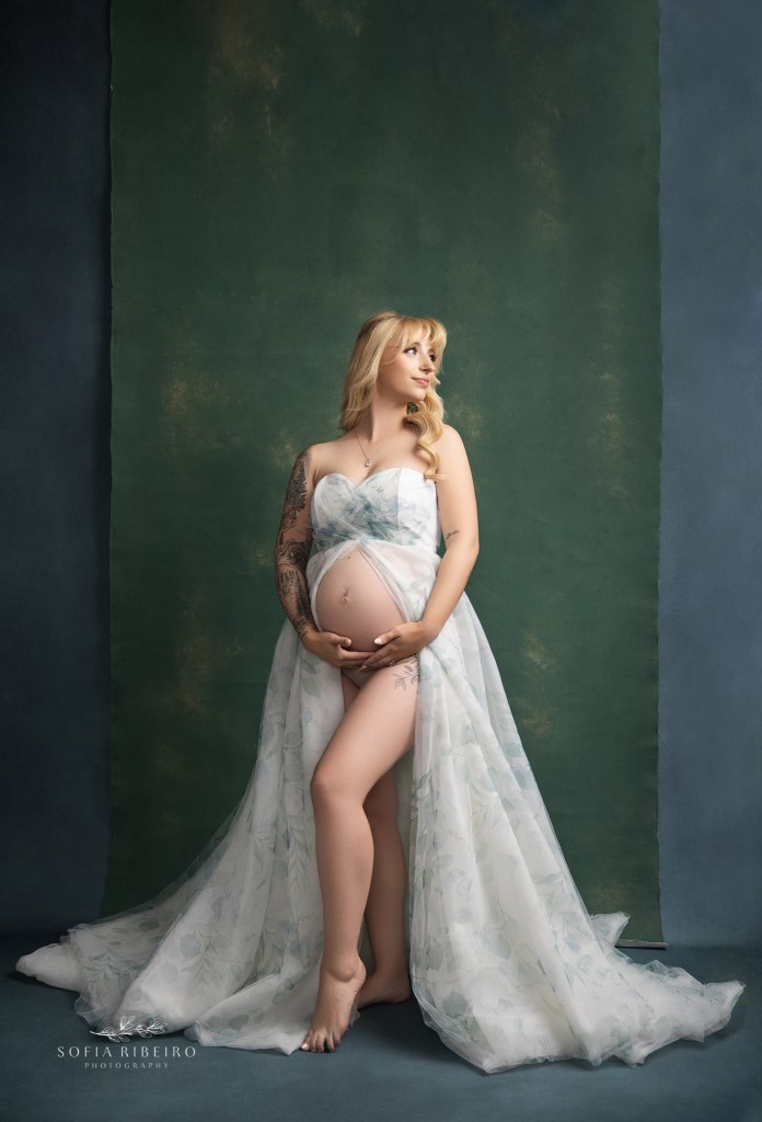 pregnant mom looks over her shoulder in a floral gown against a green backdrop