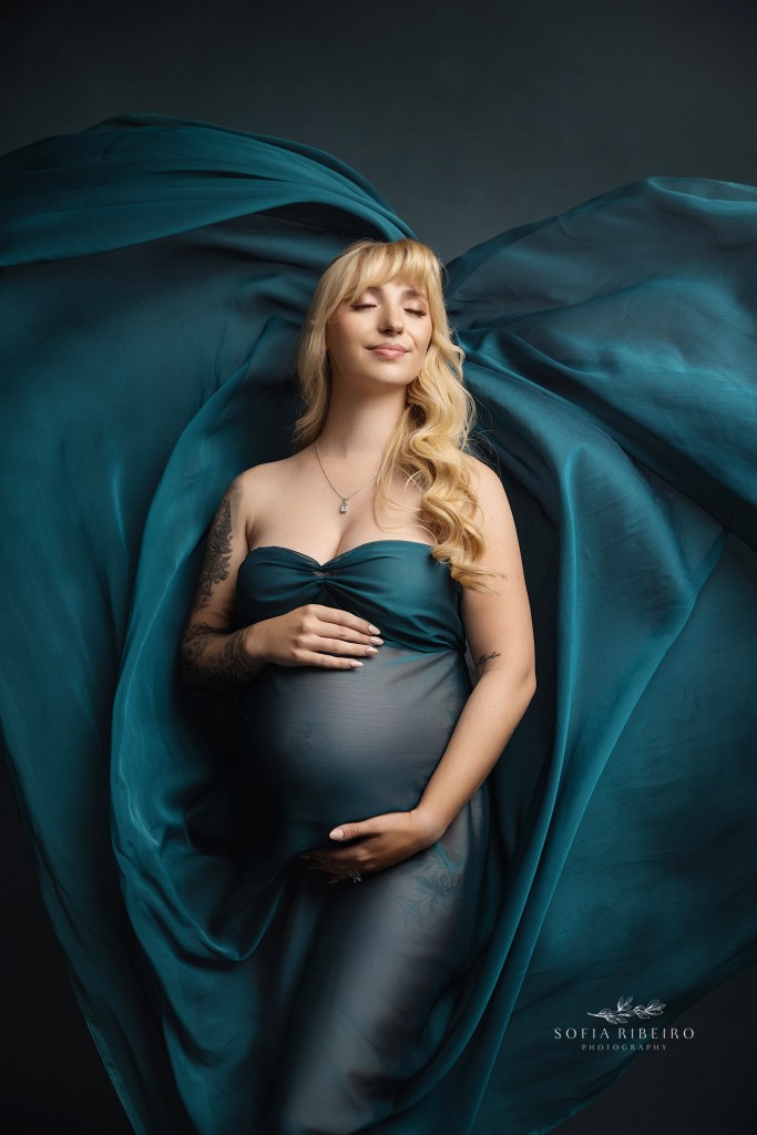 mom is draped in emerald green fabric highlighting her pregnantbelly during a maternity session
