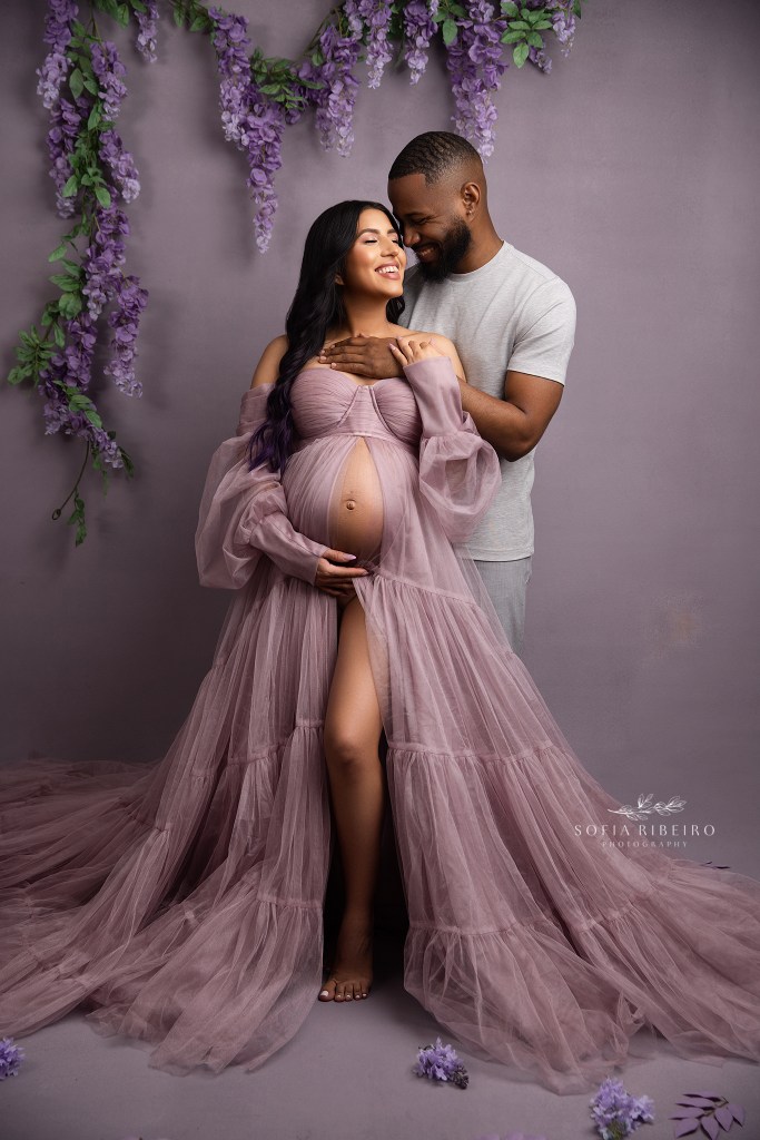 mom and dad share a sweet smile together for a maternity portrait in purple with a roselle nj maternity photographer