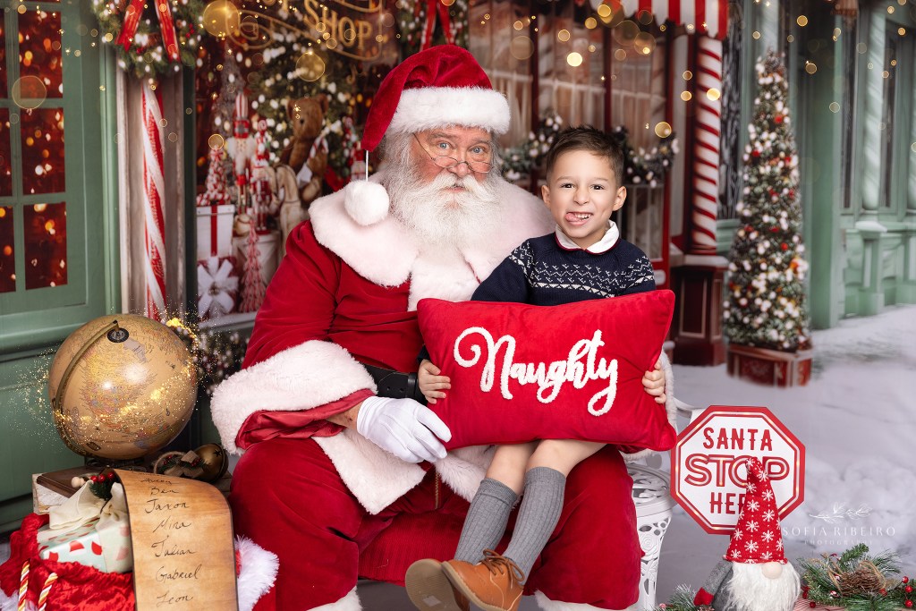 little boy shows his naughty face to santa while holding a naughty pillow for santa photos in nj