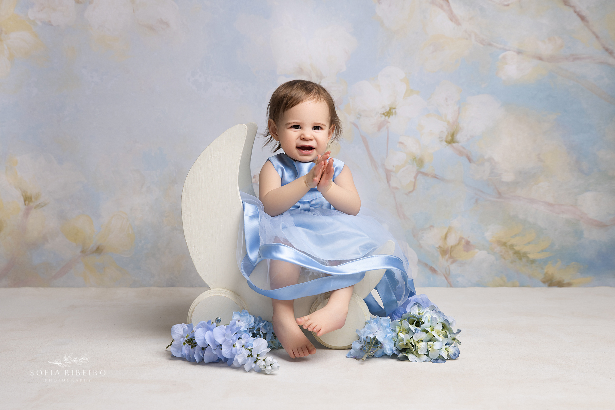 1 year old baby girl poses in a moon prop against a floral backdrop