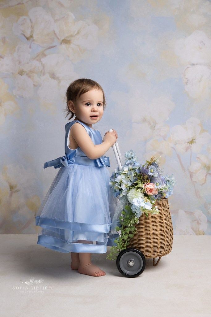 summit nj family photographer captures a 1 year old girl with a floral basket against a blue backdrop