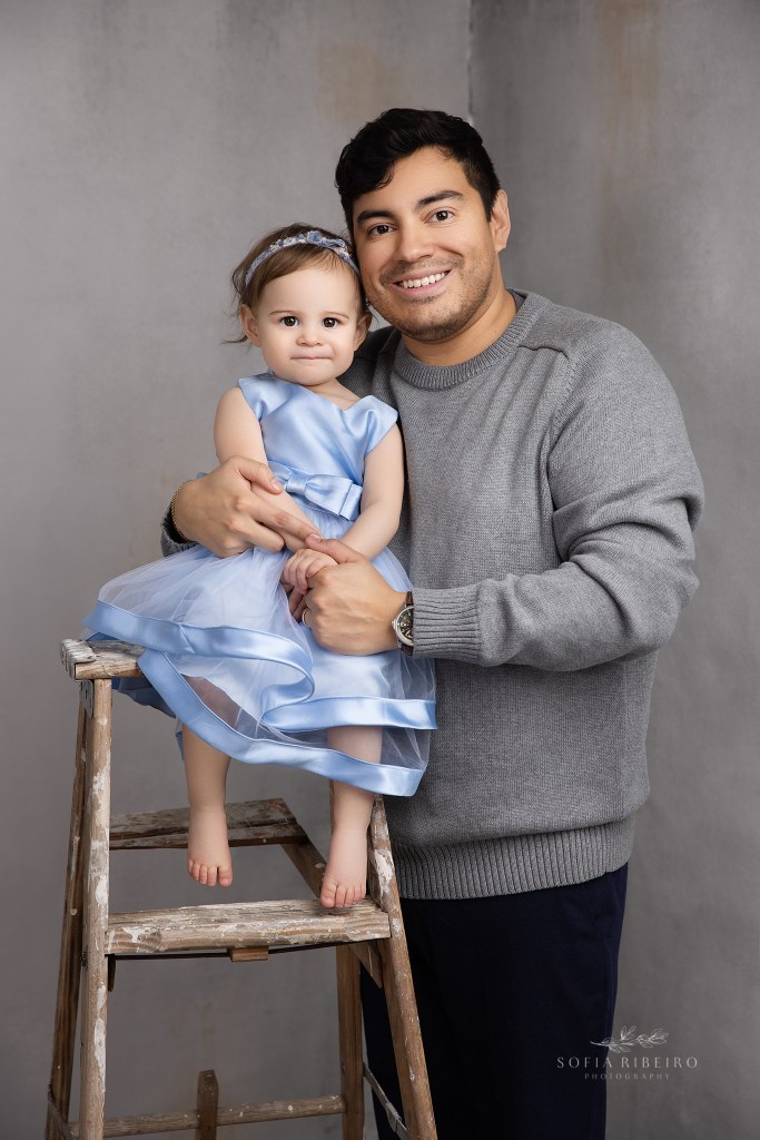 dad shares a tender moment with his daughter posed on a ladder for a portrait