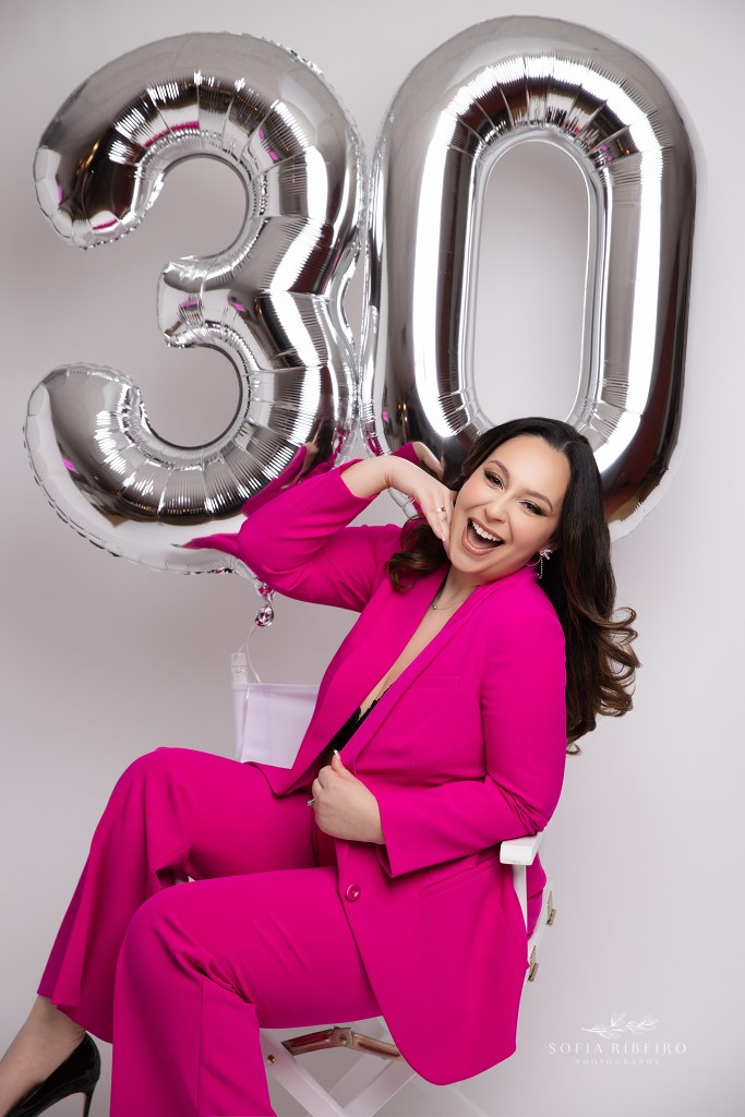 a 30th birthday portrait featuring a hot pink suit and silver number 30 balloons in a white chair during a portrait session with a nj photographer