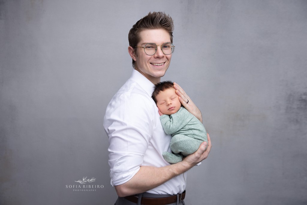 dad smiles proudly, holding his baby boy in his arms