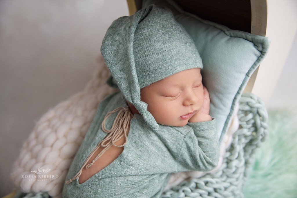 a sweet newborn baby boy snuggled on a sage green pillow and matching outfit