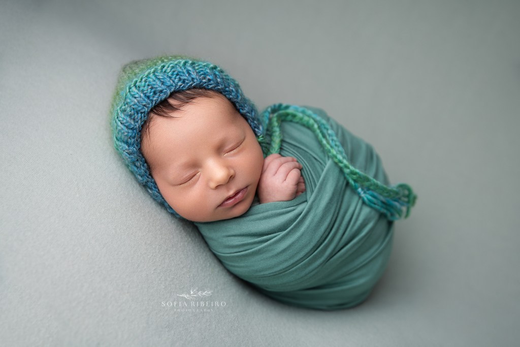 newborn baby boy is wrapped in a teal wrap on matching backdrop for a newborn session