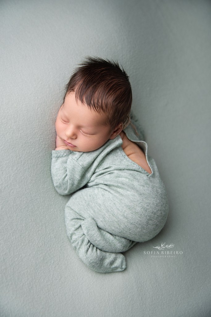 a newborn baby boy is posed in sage green fabric with a matching onesie by a dover nj newborn photographer