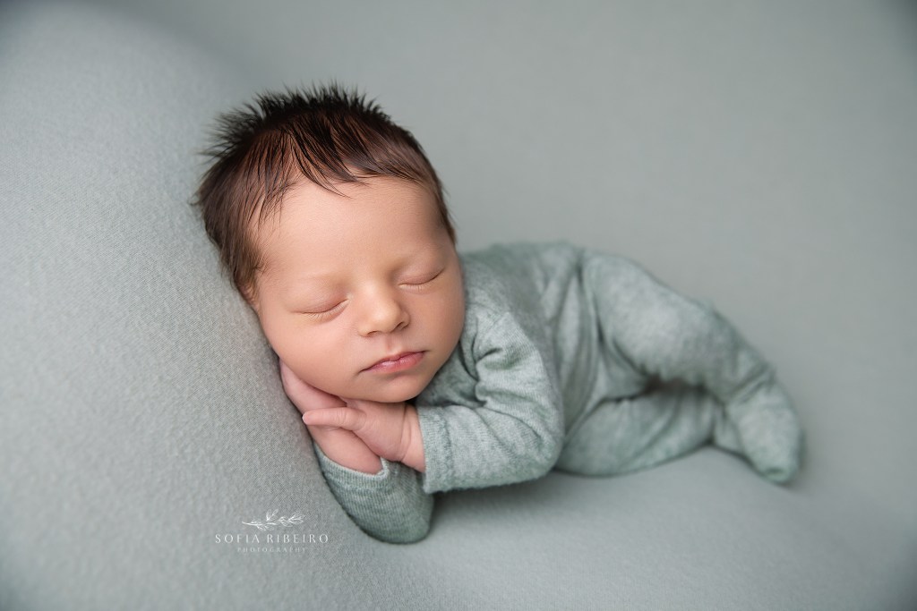 a newborn baby boy is posed in sage green fabric with a matching onesie