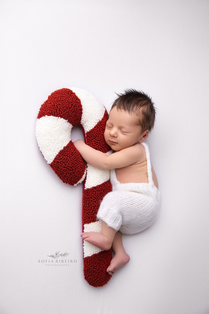 newborn baby boy snuggles a candy cane pillow for newborn photos