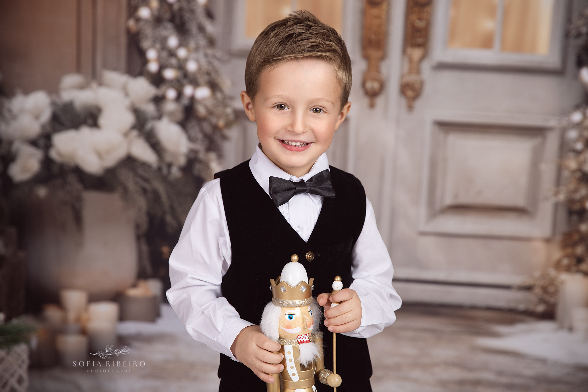 A young boy in a black vest and bowtie stands with a nutcracker on a porch during Indoor Activities For Kids in NJ