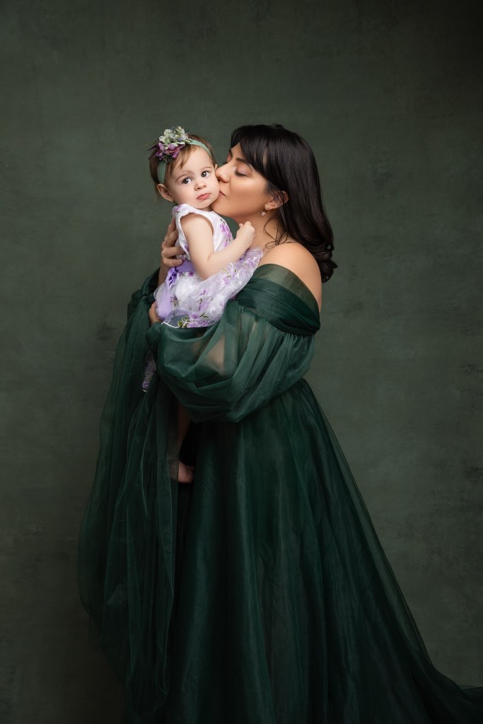 mom and baby are captured in a sweet embrace set against a green backdrop for a family photo session in nj