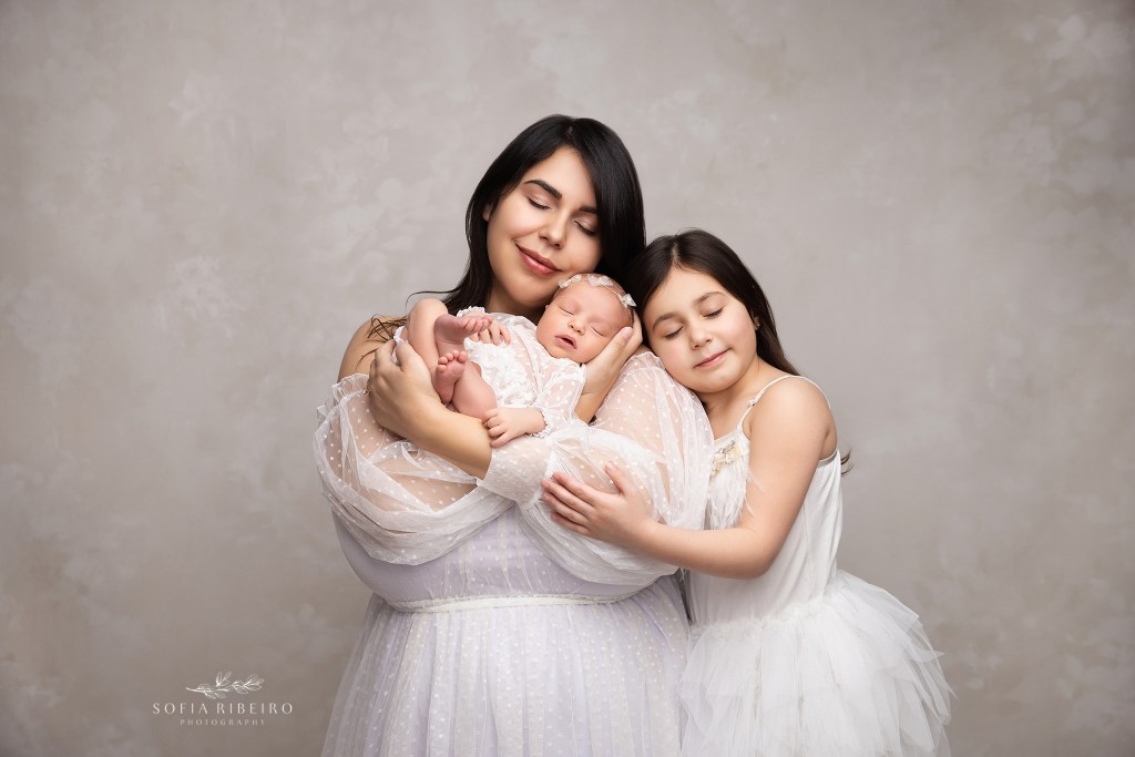 mom and big sister cradle their new little baby for a soft portrait in creams and whites in a dunellen nj newborn photographer's portrait studio