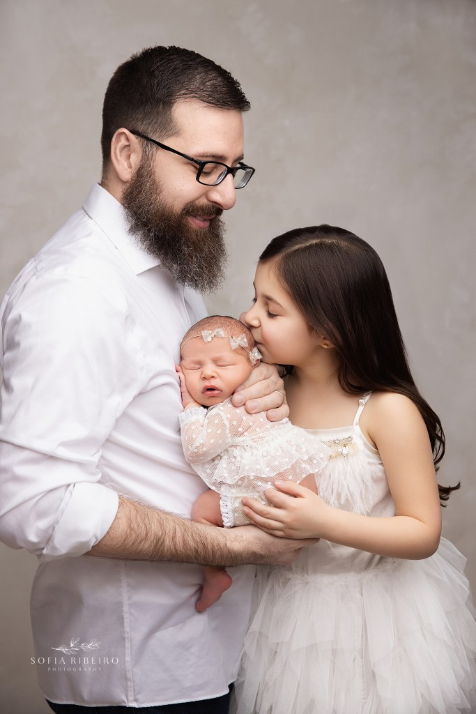 big sister kisses her baby sister while dad holds her for a sweet photo
