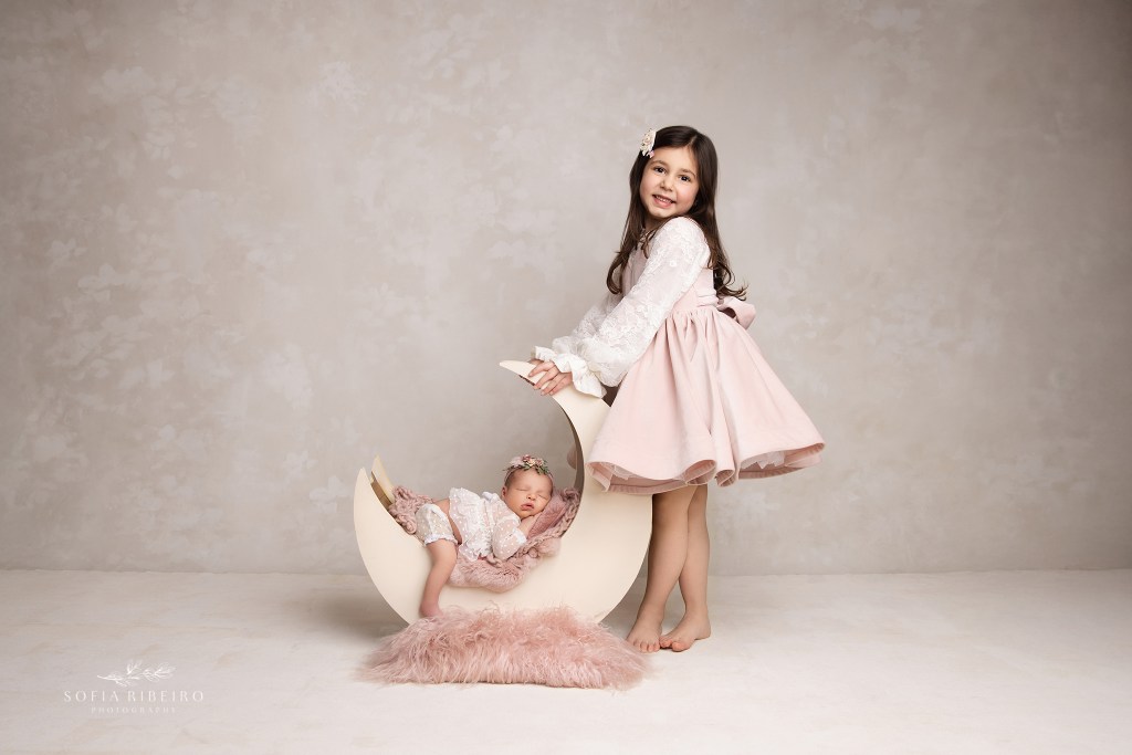 dunellen nj newborn photographer poses a newborn sweetly sleeping in a moon prop with her older sister standing by