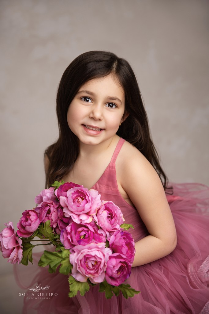 a stunning portrait of big sister in shades of pink holding a floral bouquet of pink roses