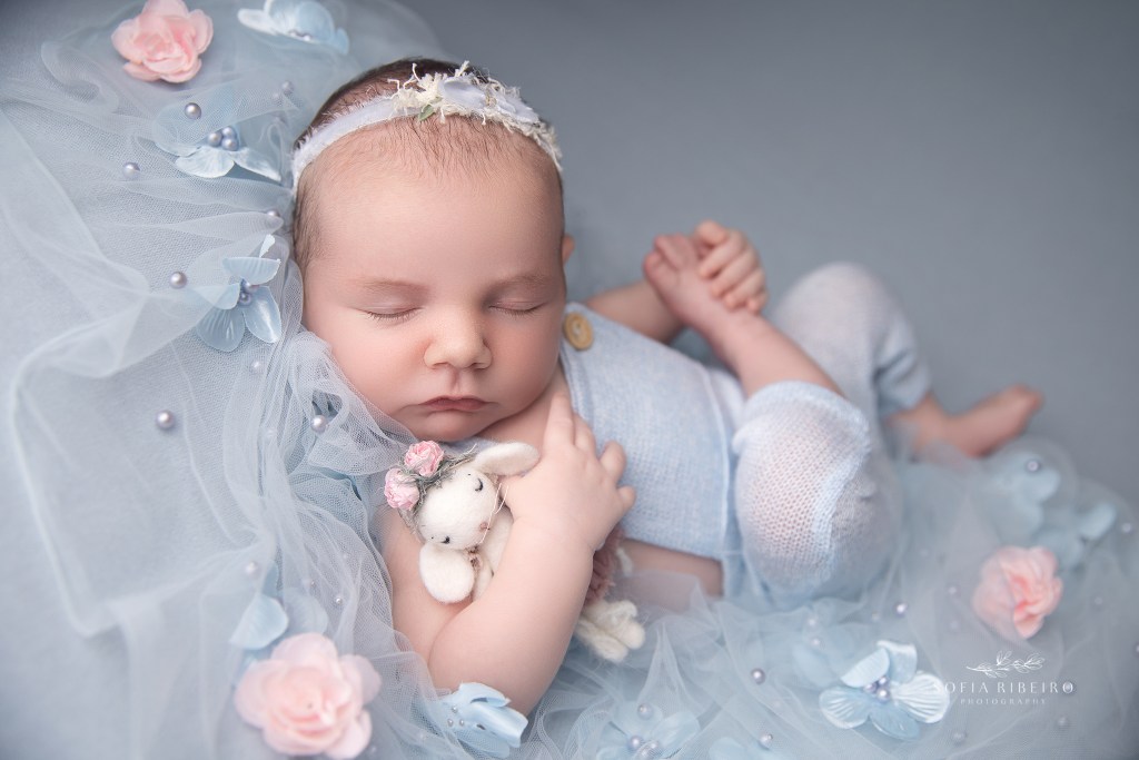 a baby girl is posed in light blue and pink shades with s tiny stuffed toy by a nj newborn photographer