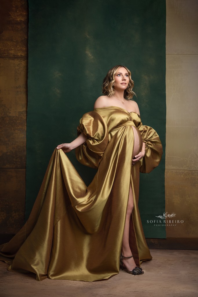 mom is draped in a gold gown against an emerald backdrop in a weehawken nj maternity photographer's studio