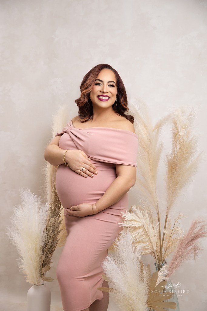 a closeup of expectant mom showcasing her baby bump in a light pink dress