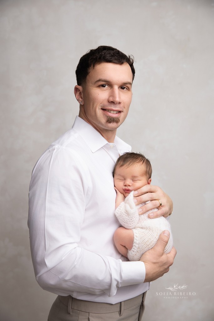 dad smiles to camera with his newborn baby boy in a proud moment