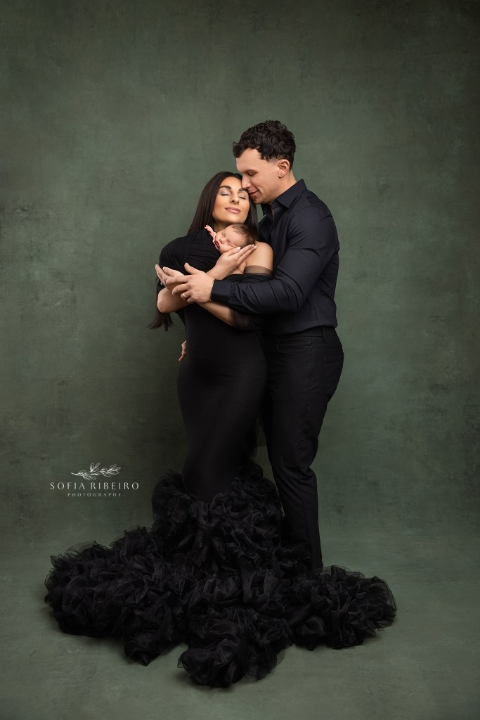 berkeley heights nj newborn photographer poses parents together with baby in elegant black outfits against a green backdrop