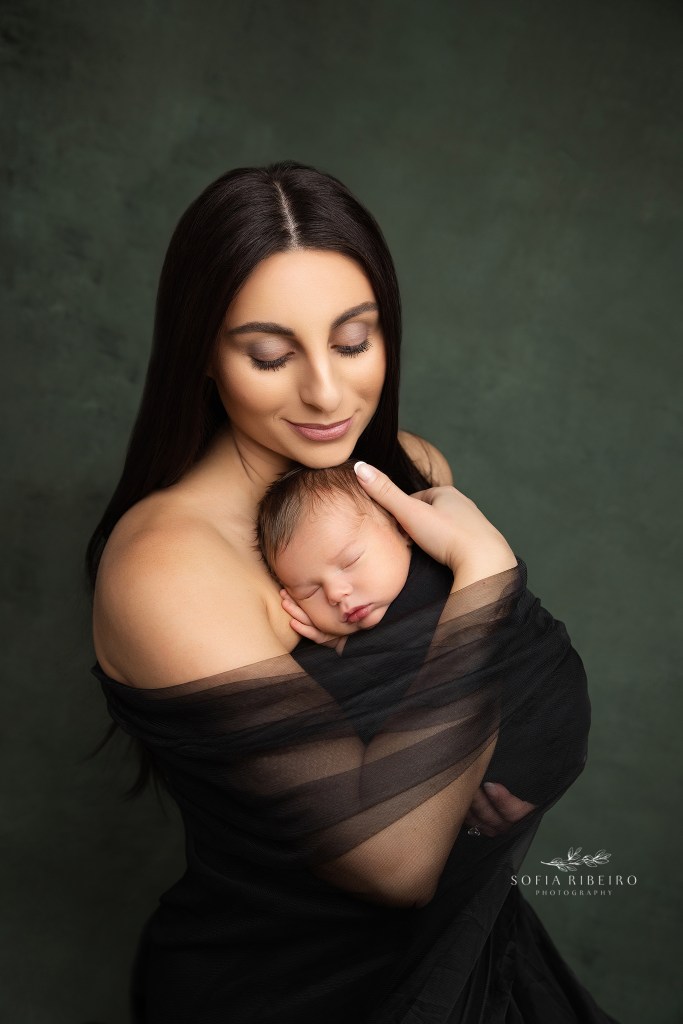 an intimate portrait of mom and baby wrapped in black tulle against a green backdrop with her newborn baby boy