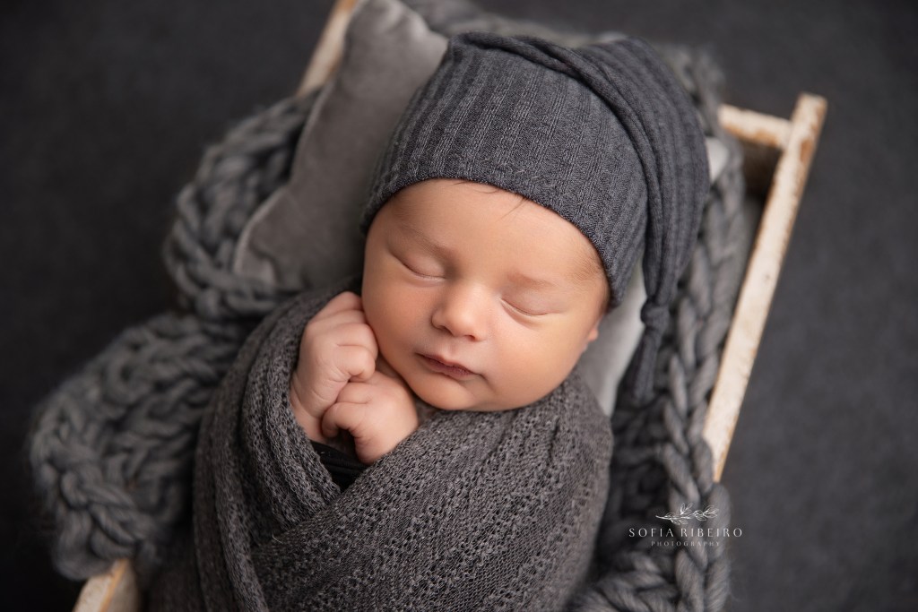 baby boy is posed in a box prop in charcoal grey wrap and matching bonnet against a grey backdrop by nj newborn photographer