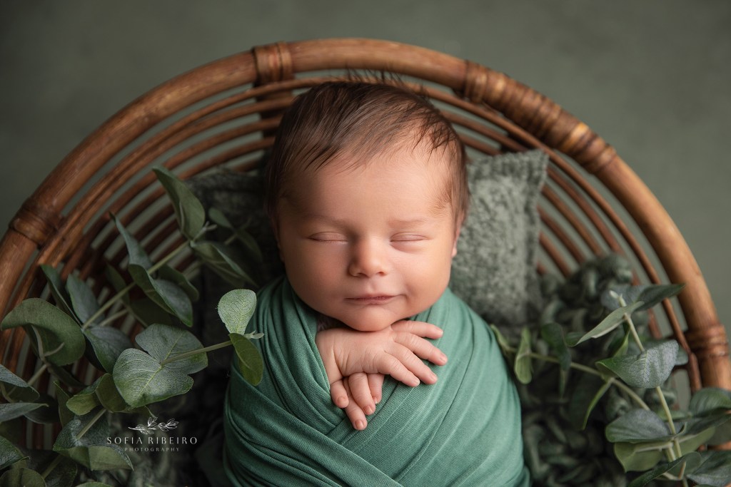 a closeup of a baby boy smiling with his hands by his chin