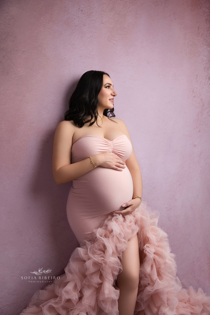 mom is posed against the wall in a mermaid gown highlighting her baby bump in hudson valley ny maternity portrait studio