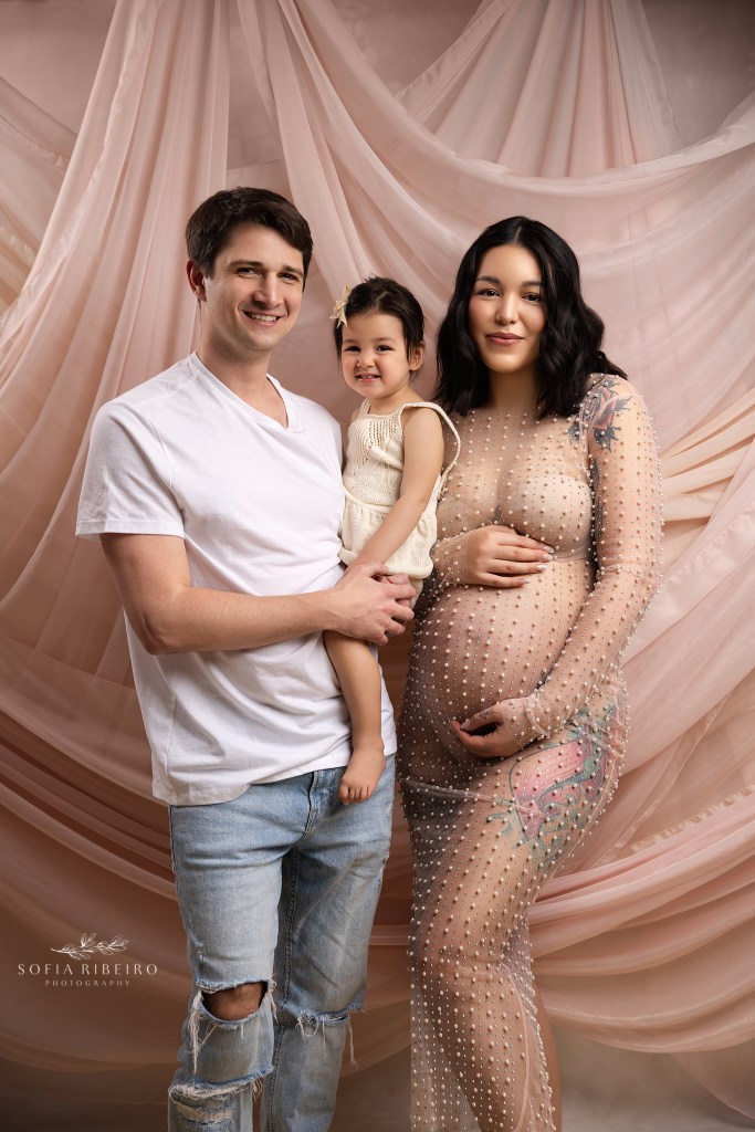 A family of soon to be four, poses for a maternity portrait in blush tones