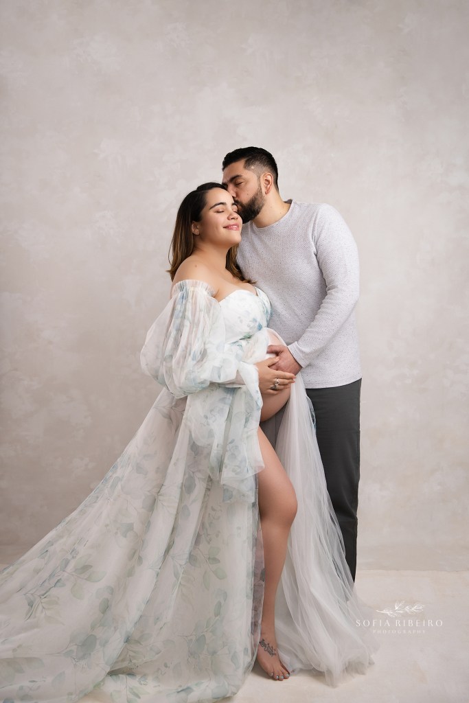mom and dad pose together sharing a sweet smile while cradling the baby bump