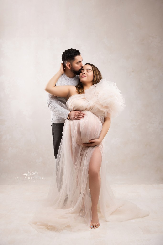a special moment shared between mom and dad, cradling baby bump against a cream backdrop by a lodi nj maternity photographer