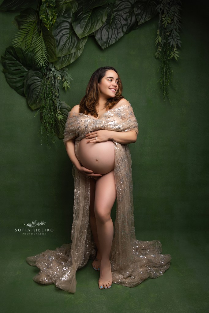 mom is draped in shimmery gold fabric highlighting her pregnant belly against a deep green backdrop