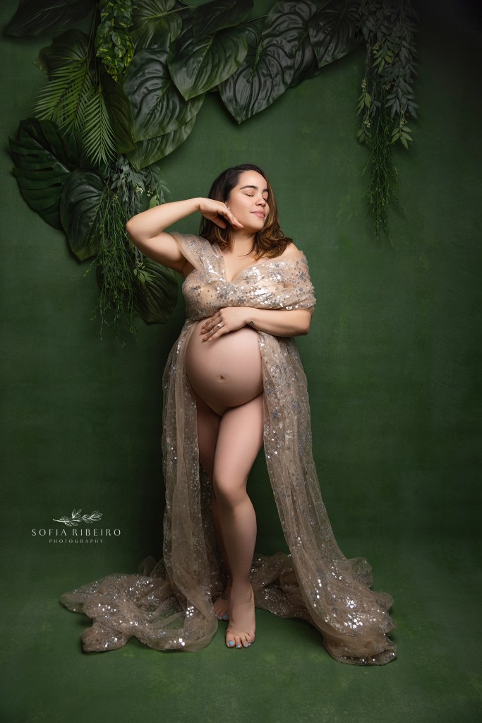 mom is draped in shimmery gold fabric highlighting her pregnant belly against a deep green backdrop in lodi nj
