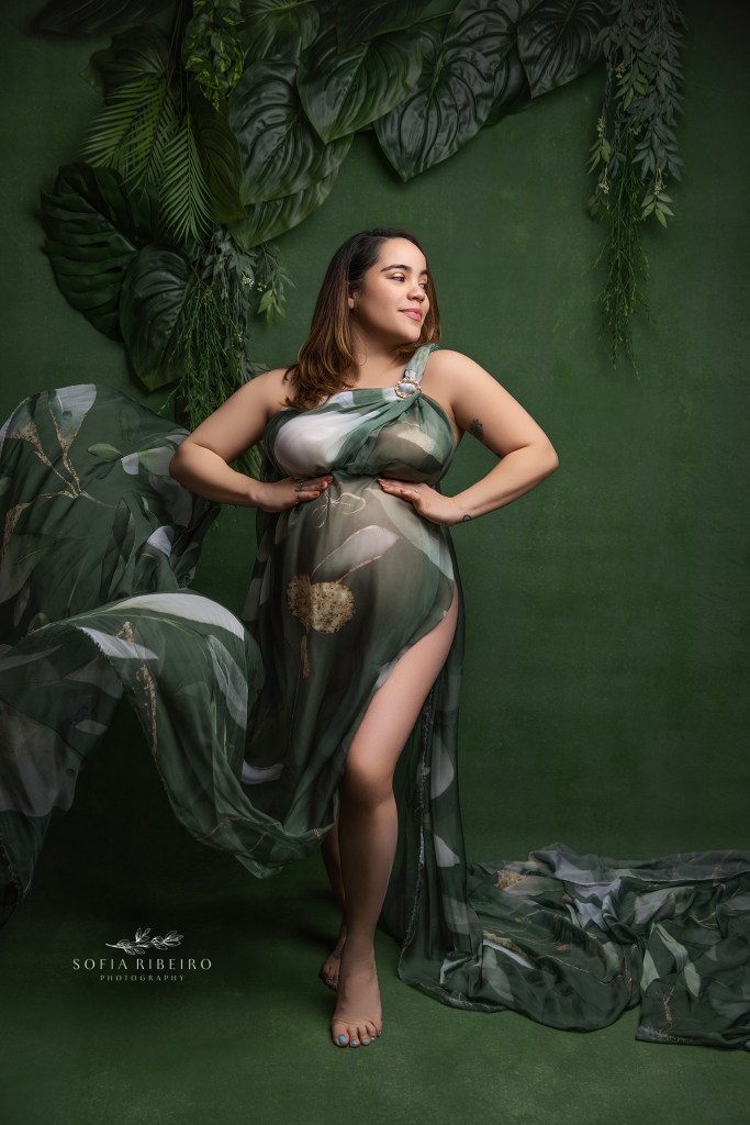 a tropical green flowing fabric curves around mom's expectant belly against a green topical backdrop