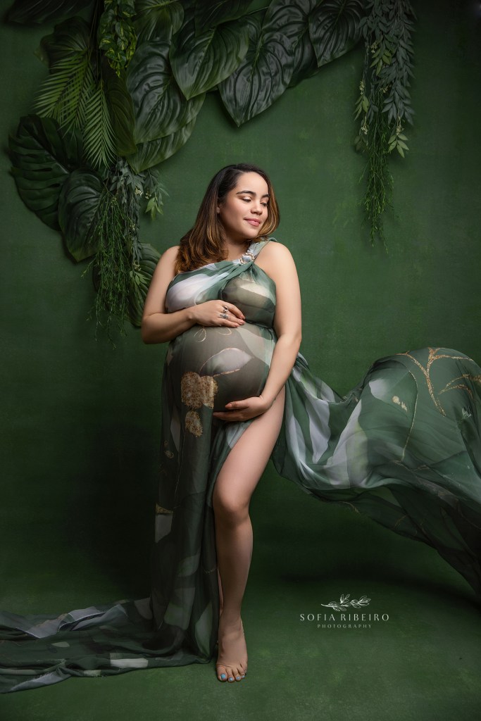 a tropical green flowing fabric curves around mom's expectant belly against a green topical backdrop
