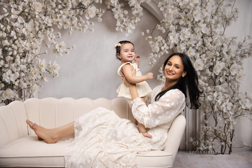 mom shares a joyous smile with her baby girl while reclined on a sofa with her baby daughter