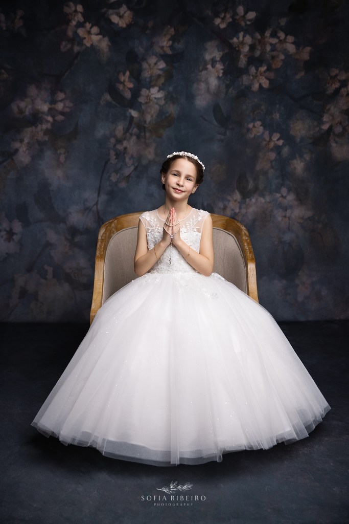westfield nj communion photographer captures a little girl in her communion dress seated in a formal chair pose against a blue floral backdrop