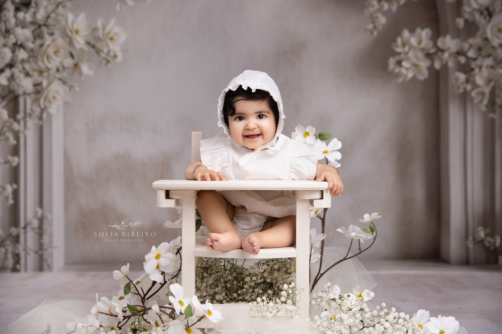 a sweet baby girl captured in a white outfit and high chair surrounded by florals