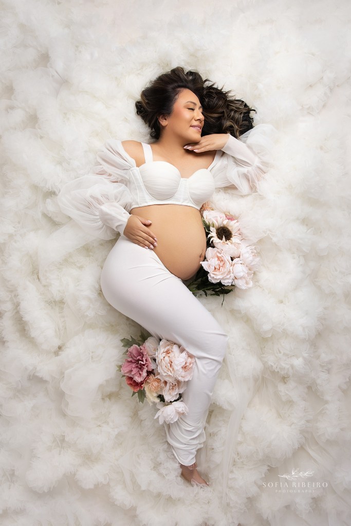 a pregnant mother is posed in a bed of white tulle ruffles exposing her belly in a serene maternity image
