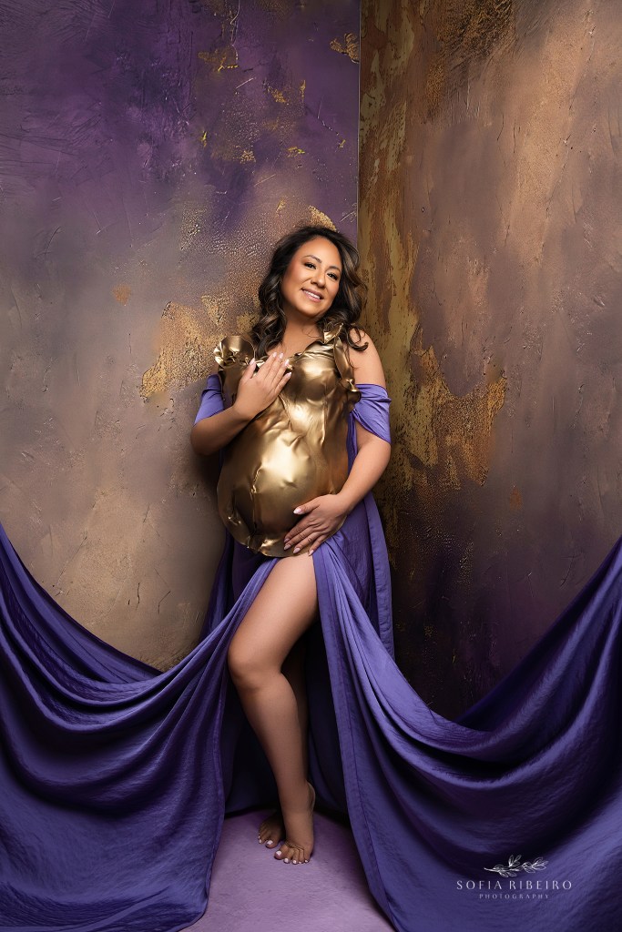 a mom is posed, hands around belly in a gold and purple themed image