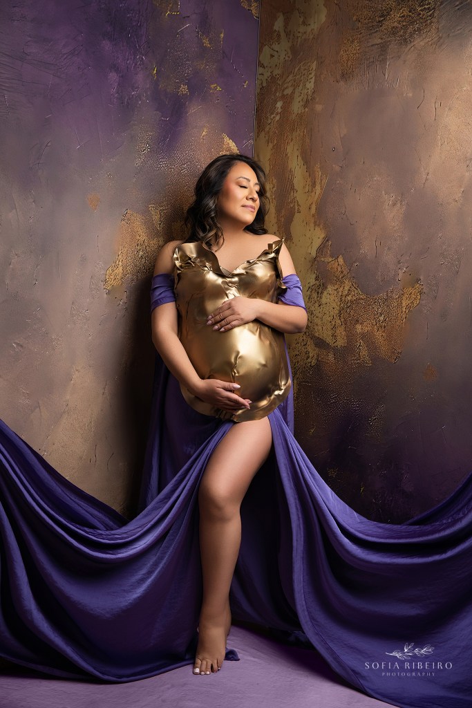 mom to be as a golden warrior with draped purple fabric and gold bust against a marbled backdrop captured by an englewood nj maternity photographer