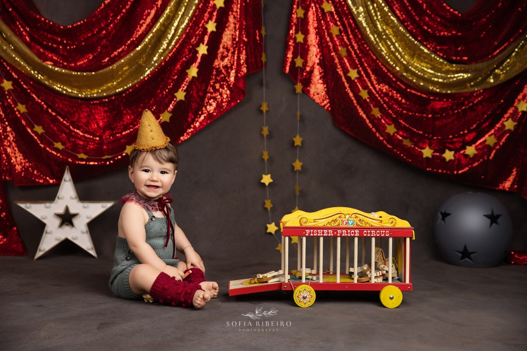 a baby in a vintage circus outfit poses for the camera with vintage toys for a monmouth county nj baby photographer