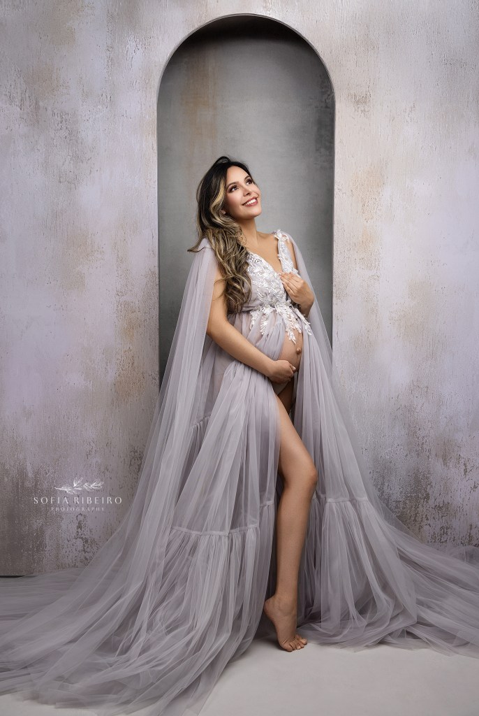 mom looks soft an radiant in a tulle grey gown, belly exposed for a maternity portrait