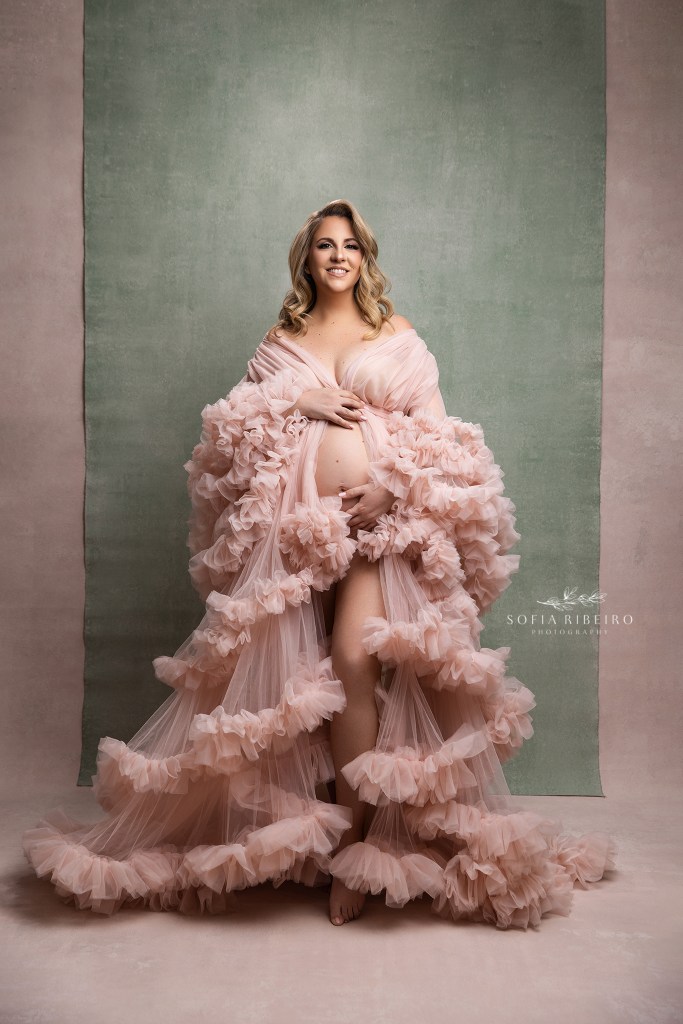 mom poses elegantly in a pink gown with sage backdrop for a soft portrait