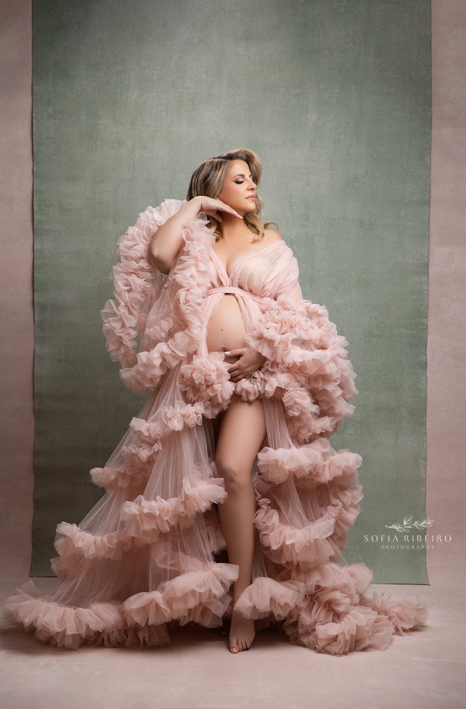 mom poses elegantly in a pink gown with sage backdrop for a soft portrait