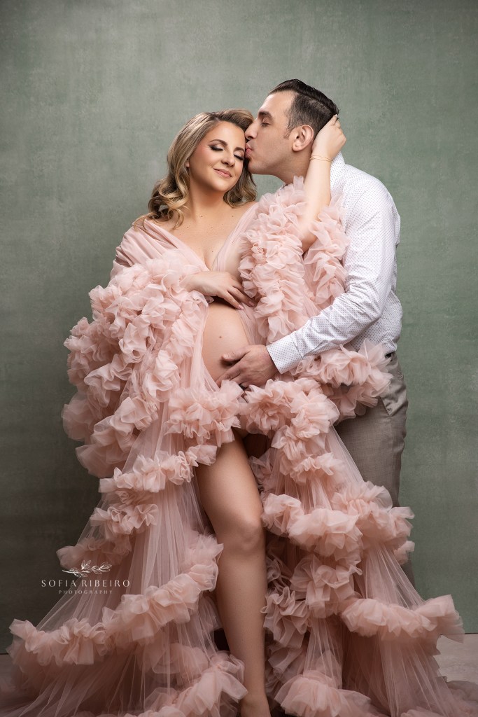 mom and dad share a sweet embrace in pink against a sage green backdrop in a middletown nj maternity photographer's studio