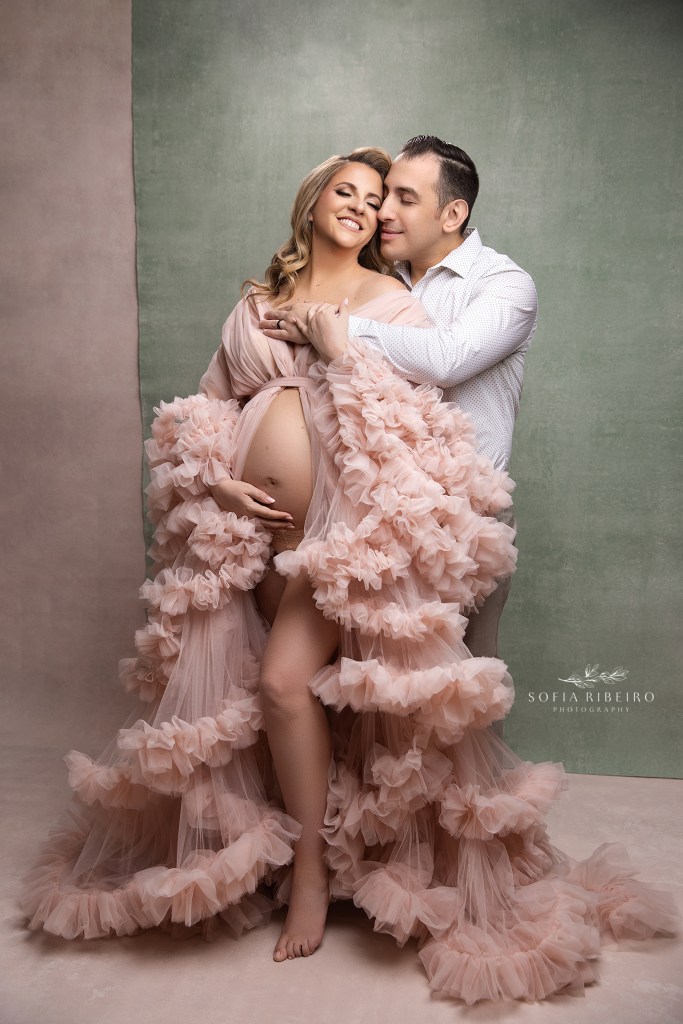 mom and dad share a sweet embrace in pink against a sage green backdrop